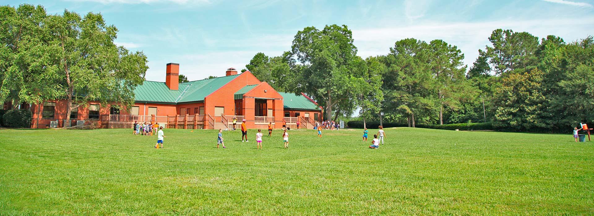 Wide shot of campers playing in field with lodge behind them at YMCA Camp Arrowhead in Suffolk, Virginia