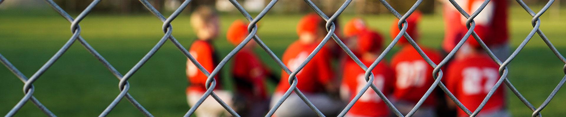 A youth sports team in red shirts out of focus on the field, looking through a chain link fence