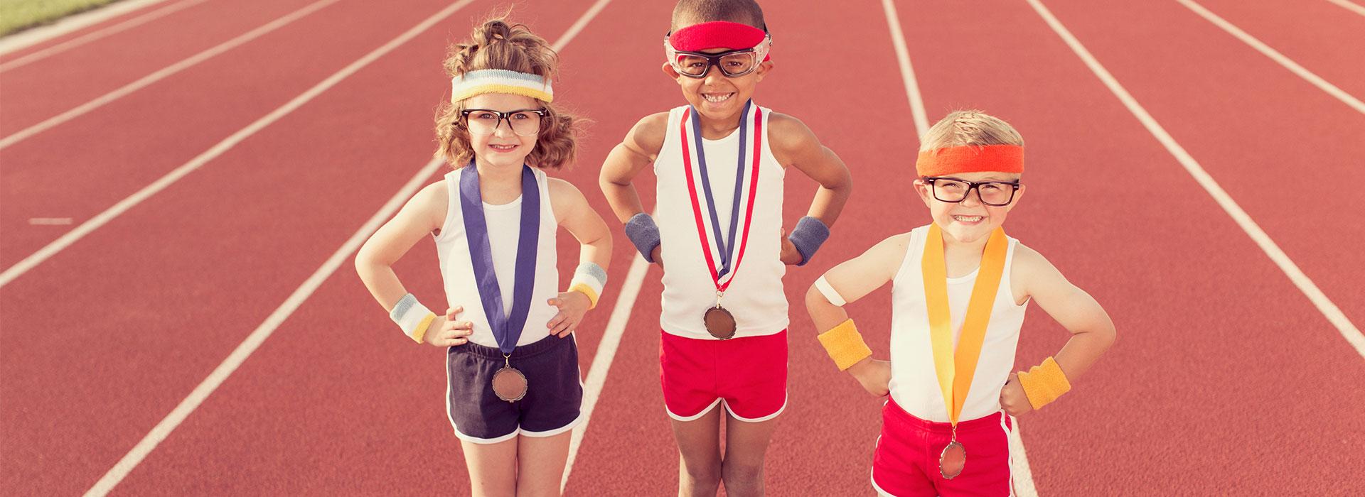 Three kids in retro athletic wear, headbands and sweatbands showing off their championship medals on a track.
