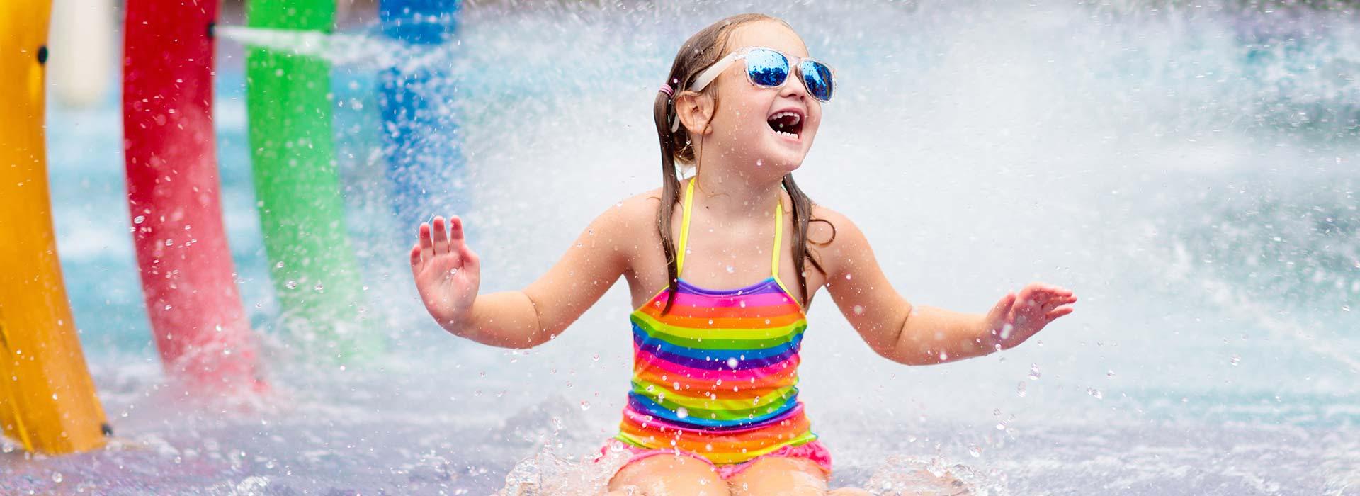 Young girl in rainbow swimsuit laughs in the water spray