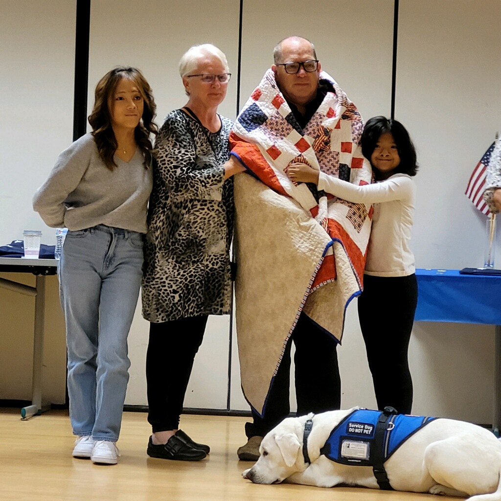 Tom Reichard and family including Norman a Labrador receiving the Quilt of Valor