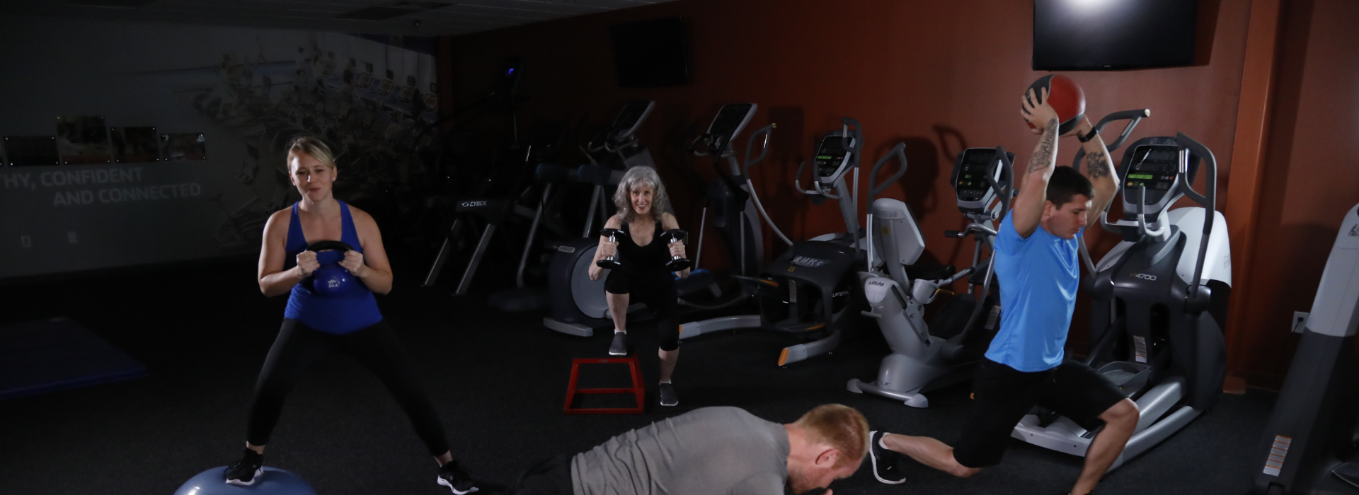 Fitness room with two men and two women working out with personal trainer