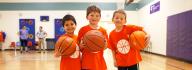 Three young YMCA basketball players holding basketballs in the indoor gymnasium at the Hilltop Family YMCA
