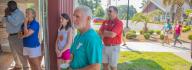 YMCA donors look on at campers sitting on the floor in the gym at YMCA at JT's Camp Grom during a counselor led activity