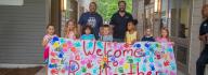 Campers and adults stand in a group holding the Welcome to Camp Red Feather sign