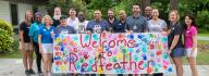 YMCA staff and donors hold the Welcome to Camp Red Feather sign