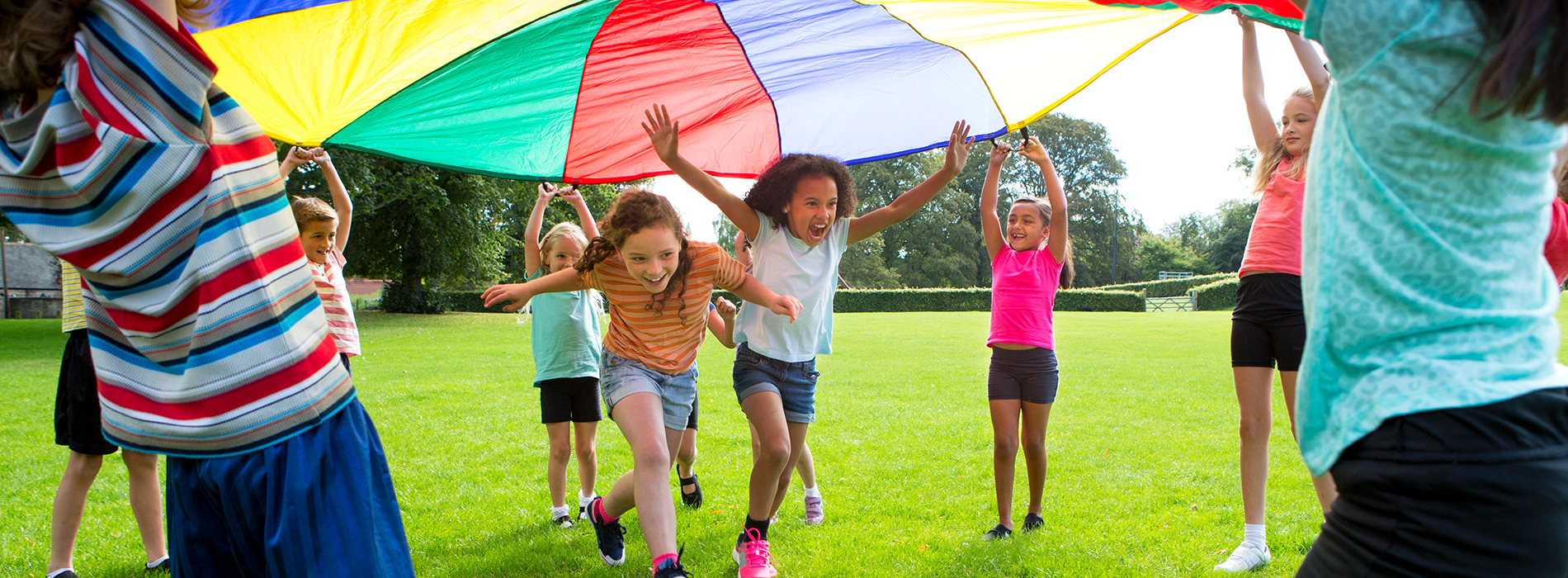 Kids playing in the grass with a multi-coloered parachute