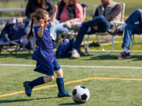 Child playing soccer having fun with parents cheering them on