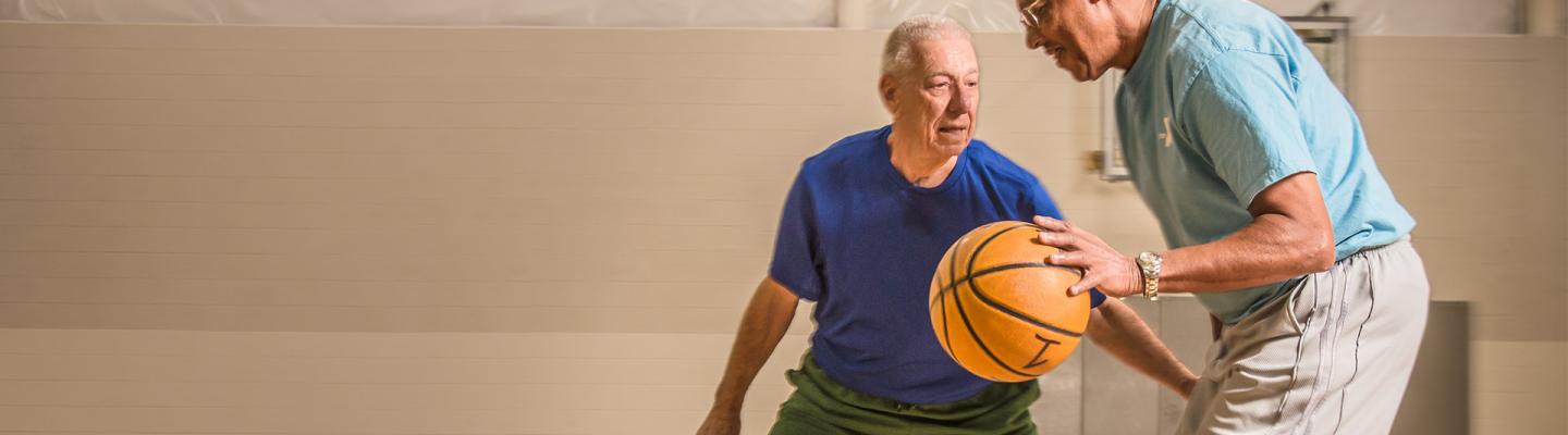 Two older adults playing 1 on 1 basketball