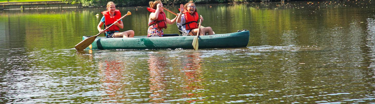 Picture of three girls canoeing in a lake, waving at the camera