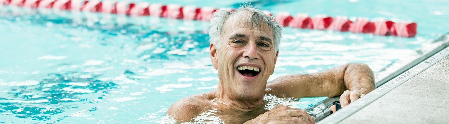 Older white male swimmer smiles at the camera at the end of the swimming pool