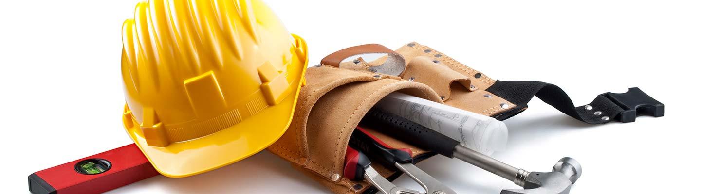 construction tools laying on a white table, including level, hard hat, and leather tool pouch with hammer, wrenches, and glue