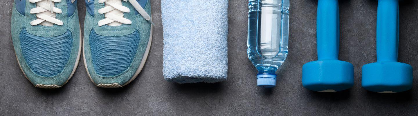 Fitness equipment on a dark floor: Sneakers, towel, water bottle, hand weights