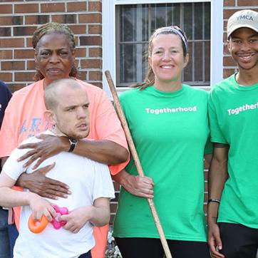 YMCA togetherhood program volunteers in green shurts standing outside in front of a brick building