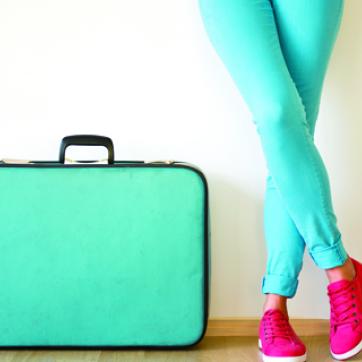 teal green suitcase with lady standing next to it in teal pants and pink shoes