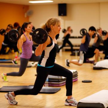 Indoor studio group exercise class lifting weights while lunging with step risers in group power.