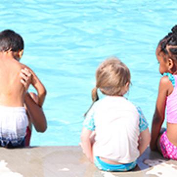 Kids sitting on the edge of an outdoor pool