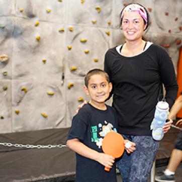 Mom and son standing in front of a rock walll holding a ping pong paddle and ball