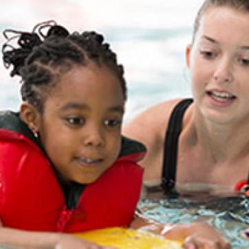 Kids wearing a red life jacket getting swim lessons