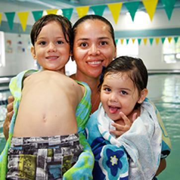 Mom with 2 kids smiling that just got out of an indoor pool
