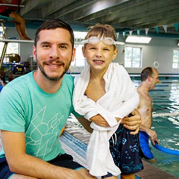 Dad with teal shirt and son with water goggles on by the indoor pool