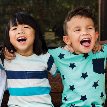 Diverse group of kids with arms around each other sitting outside in front of a brick wall