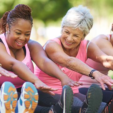 Older women wearing pink, sitting down and touching their toes