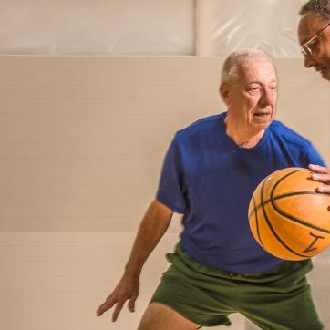Two older adults playing 1 on 1 basketball