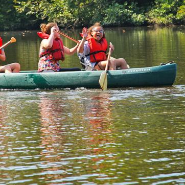 Picture of three girls canoeing in a lake, waving at the camera