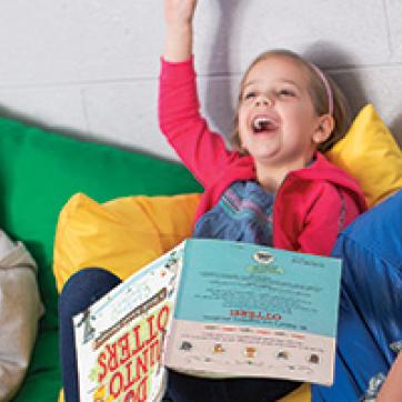 Kids resting on floor pillows and laughing in a reading corner of the Y's after-school program