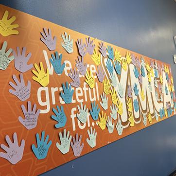 Orange banner that reads "We are grateful for.... YMCA" with paper handprints attached where members and staff have shared what they are grateful for.