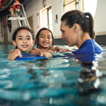 Two girls smiling with YMCA swim instructor in the pool