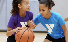 Two young girls playing basketball in a YMCA gym