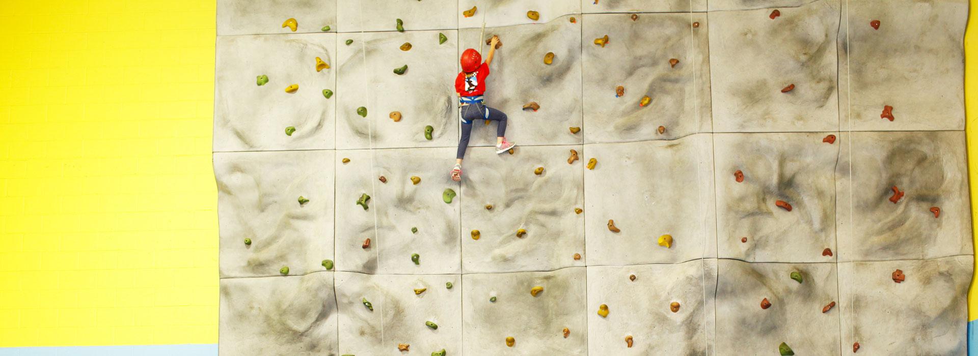 A child in safety harness climbing the rock wall at the Albemarle Family YMCA