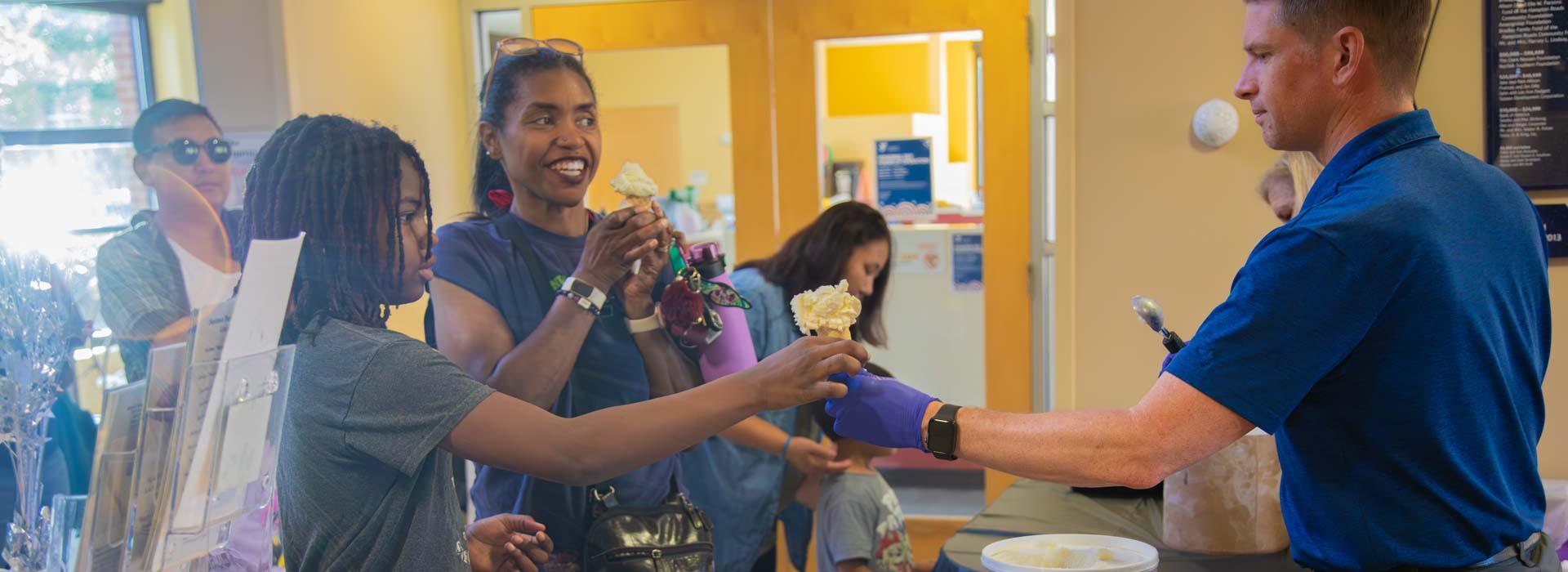 Parents and children smile at volunteers while waiting for ice cream cones