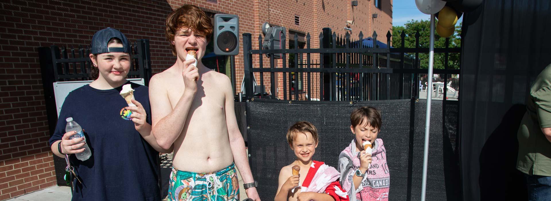 Children smile and enjoy ice cream cones in front of the YMCA on Granby's pool fence