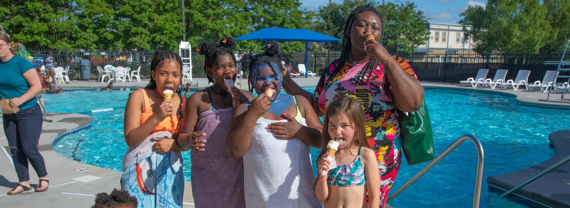 Swimmers stand in front of the pool enjoying ice cream cones