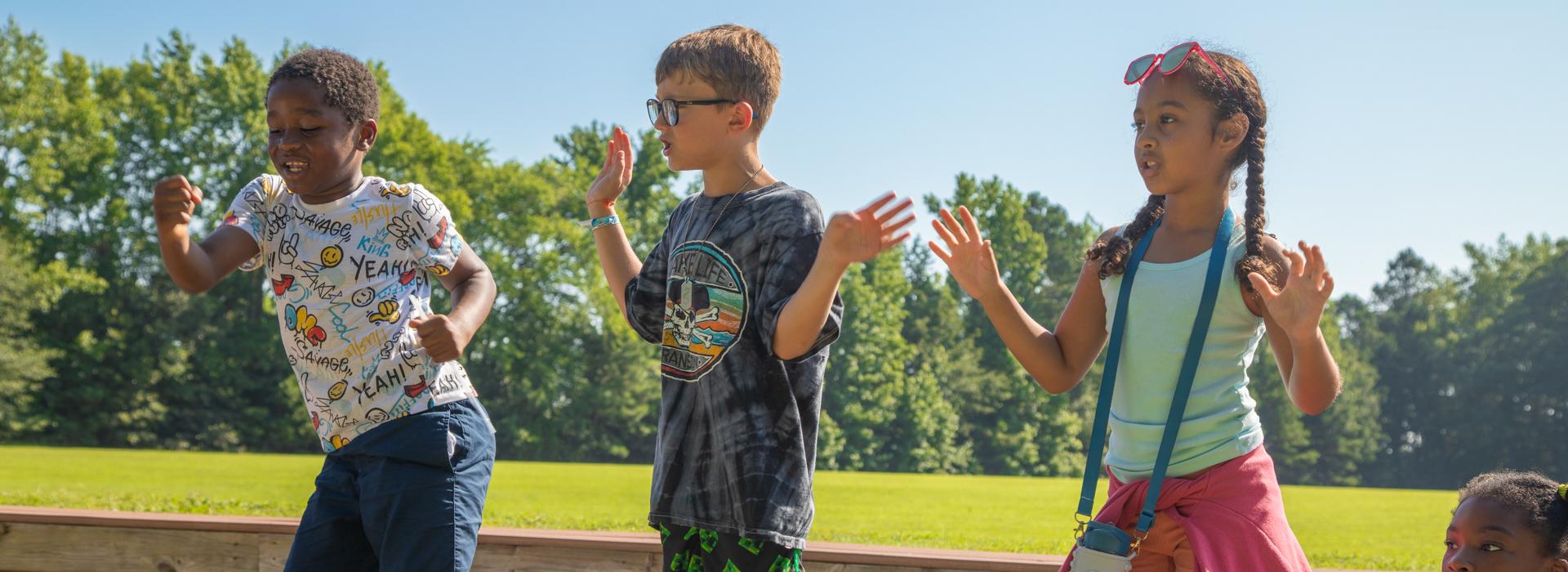 Three Camp Arrowhead campers lead an activity with arms in the air during opening ceremony