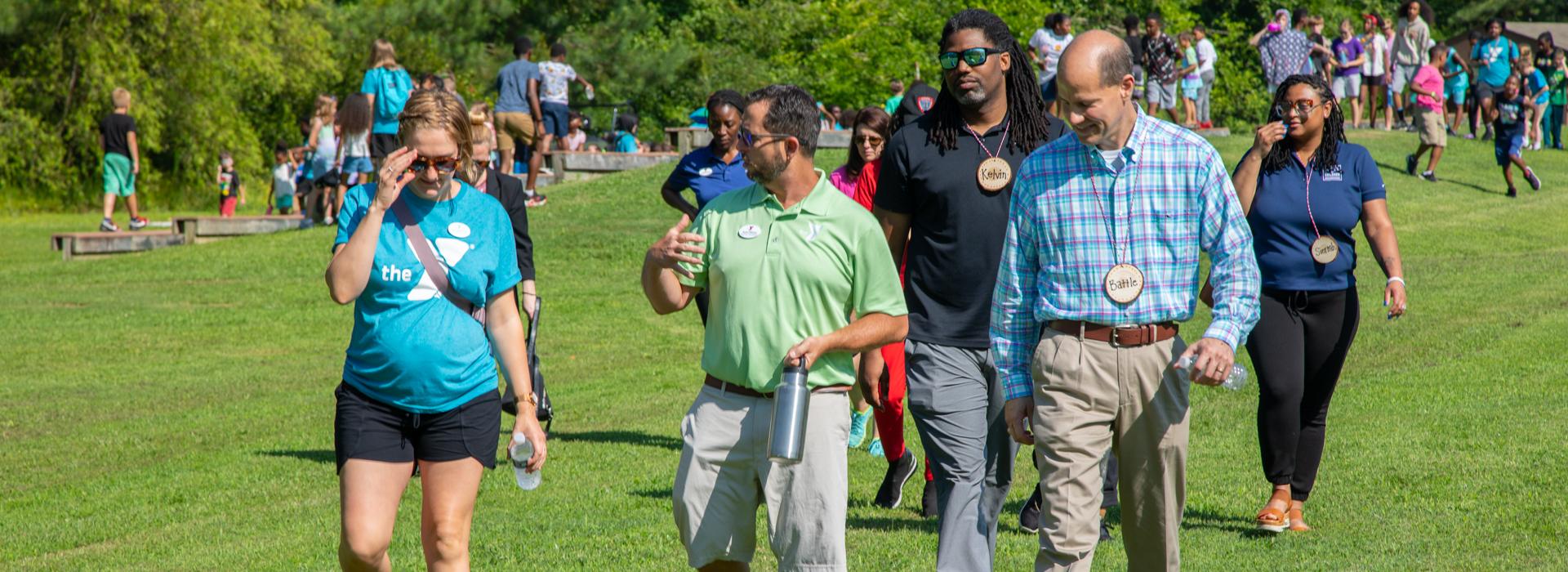 YMCA donors and staff walk across the camp while campers play in the background