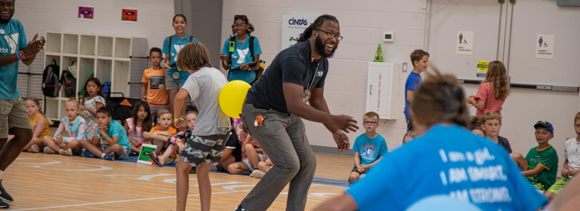 YMCA at Jt's Camp Grom counslor and camper play a game with a rubber ball between their backs while other campers watch