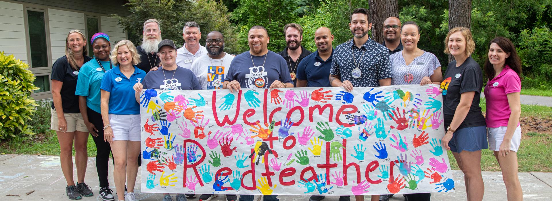 YMCA staff and donors hold the Welcome to Camp Red Feather sign