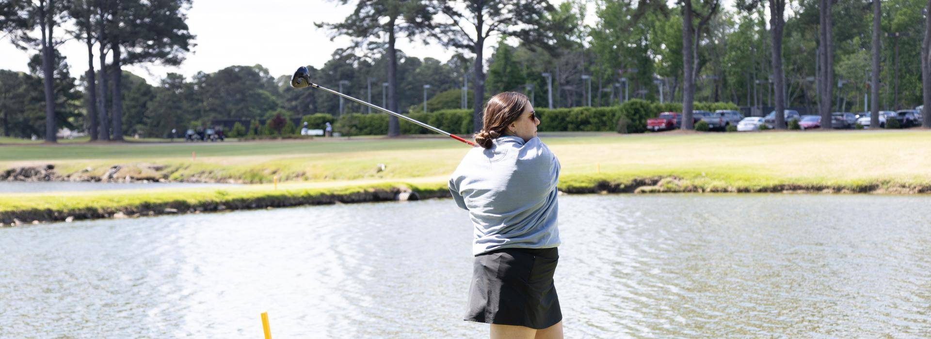 Woman swinging a golf club on the golf course with a pond in the background