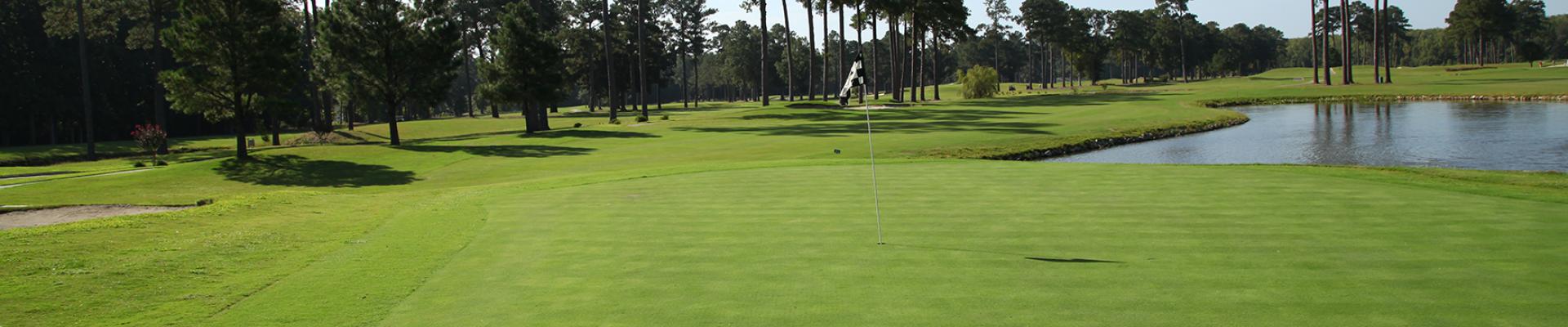 Green with flag, trees and lake in background at YMCA at the Pines, 18-hole golf course in Elizabeth City, NC
