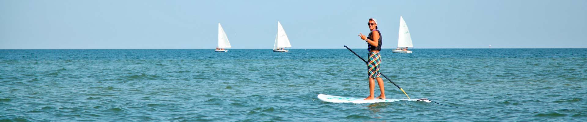 Paddle boarder on the Chesapeake Bay at YMCA Camp Silver Beach, with sailboats in the background