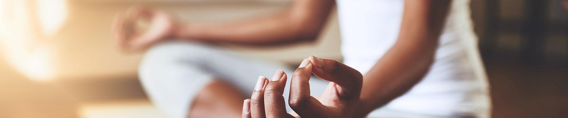 Close up of knees and hands of person sitting cross-legged on yoga mat