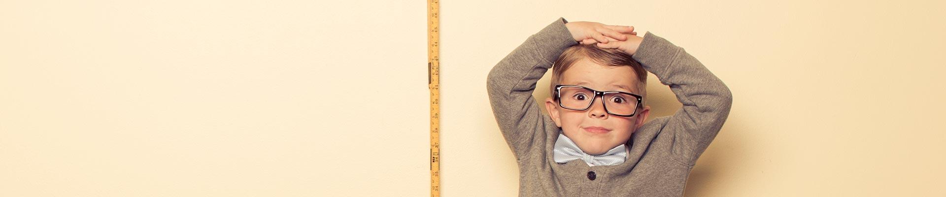 Young child in glasses and bow tie measuring height against a wall