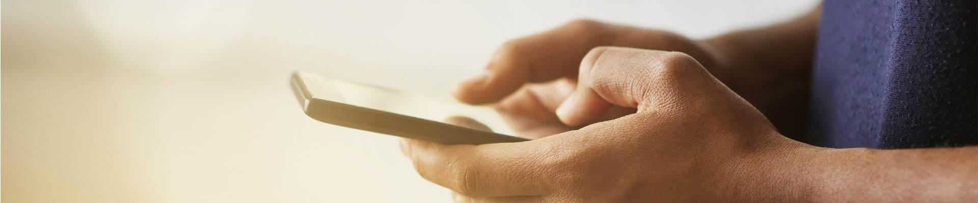 Hands holding a cell phone, thumbs interacting with the screen