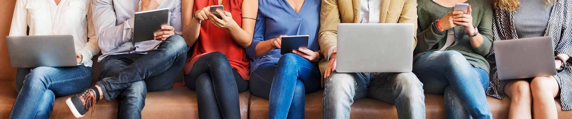 Row of people sitting, using laptops, tablets and phones