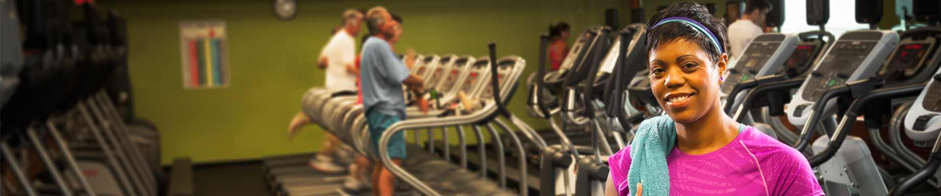 YMCA member smiles at the camera with treadmills, bikes and ellipticals in the background