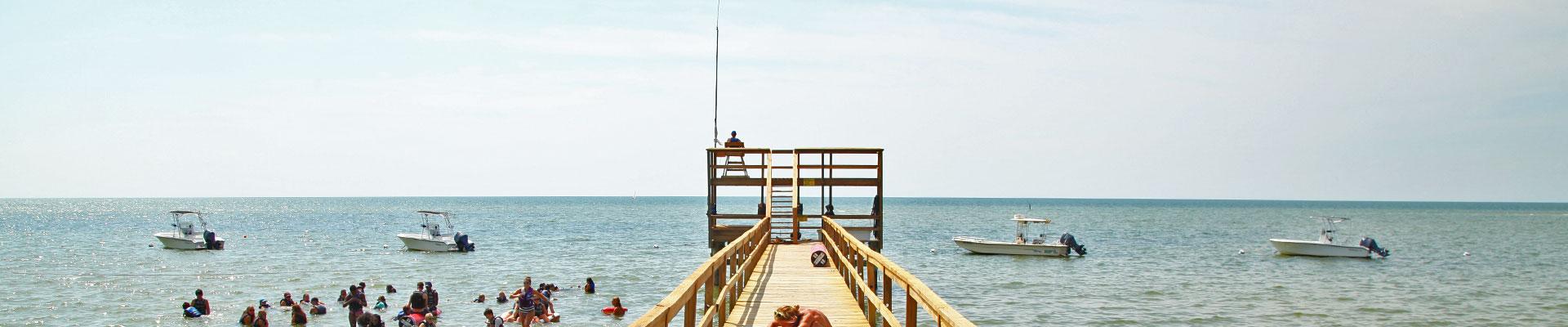 Campers playing in the Chesapeake Bay with fishing pier and boats in the water